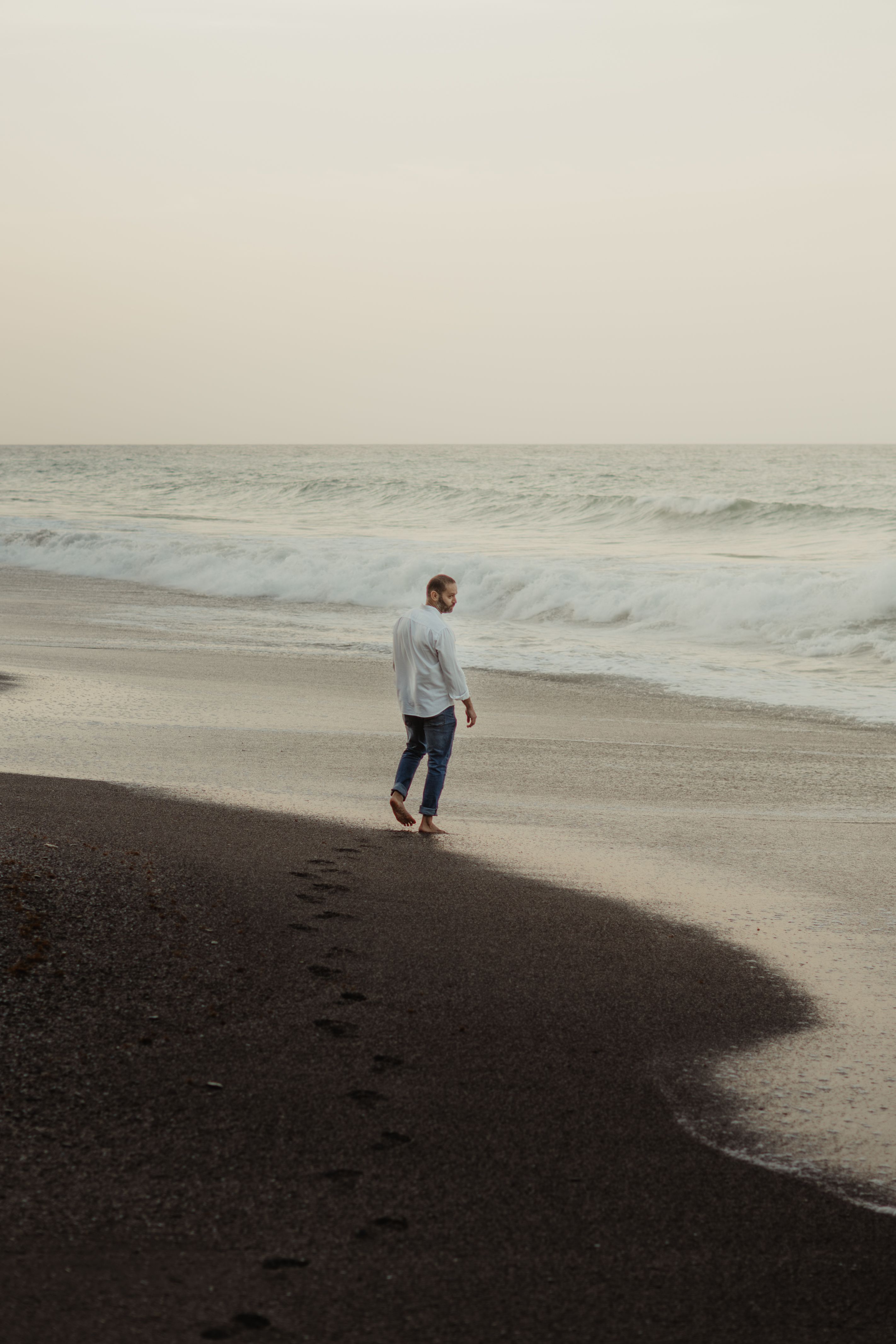 A man strolling along Anare Beach in Venezuela at sunset, leaving footprints in the sand.