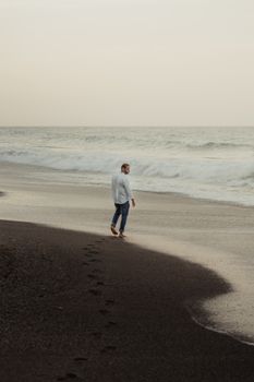 A man strolling along Anare Beach in Venezuela at sunset, leaving footprints in the sand.