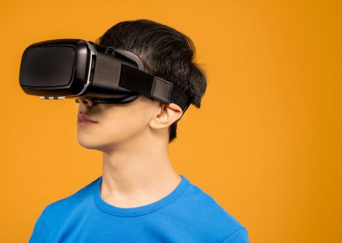 A young man wearing a VR headset immerses in virtual reality against a vibrant orange background.