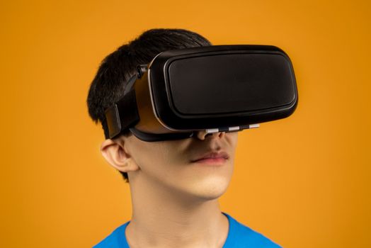 Young man immersed in virtual reality using VR headset against a vibrant orange background.