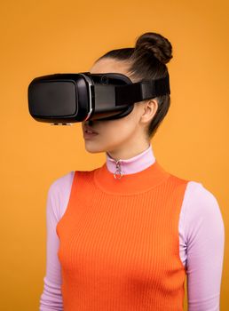 Woman wearing a VR headset and orange sweater against orange background.