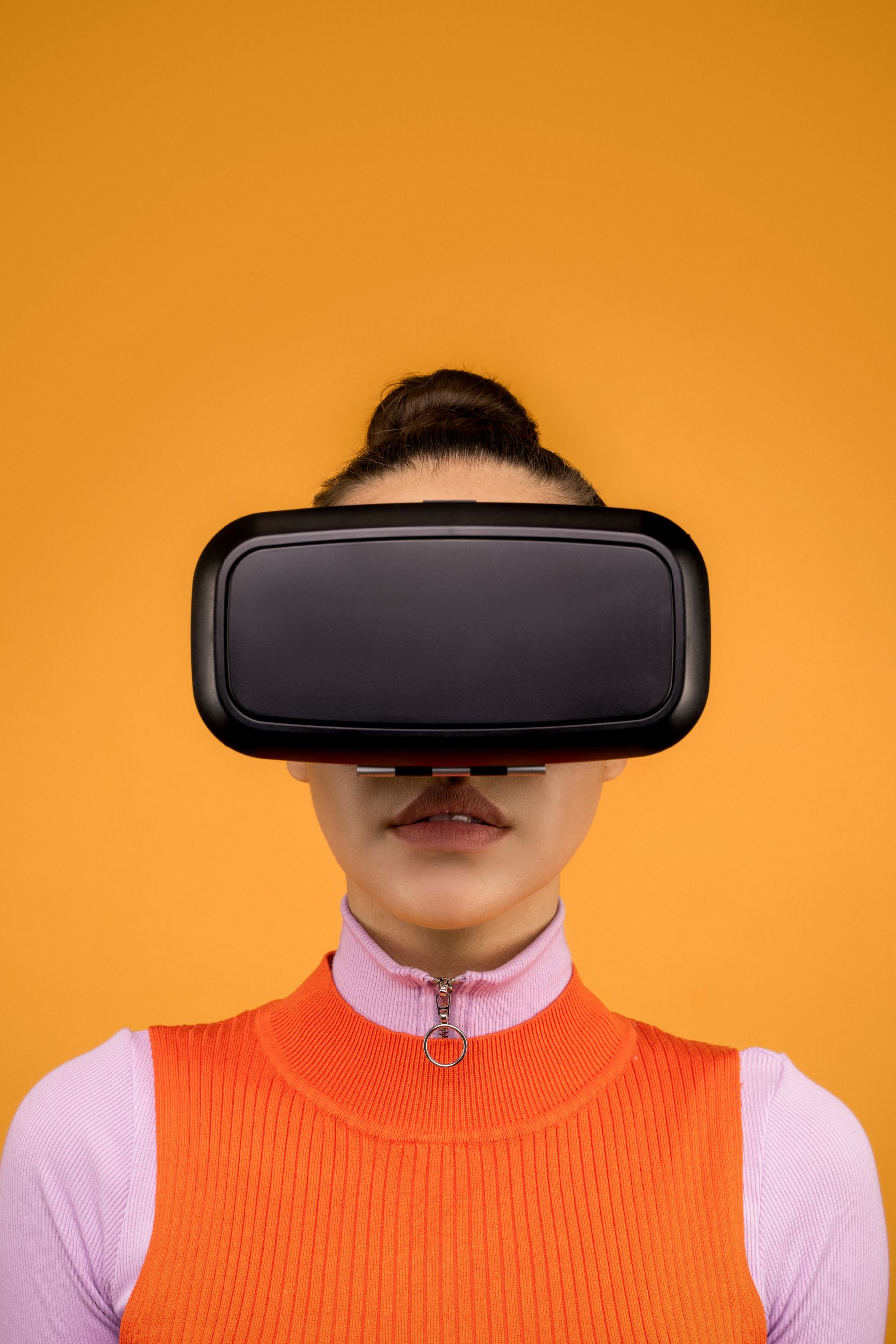 Woman wearing virtual reality goggles against an orange background