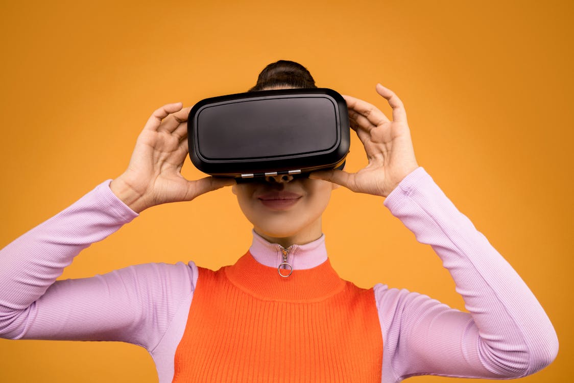 Free Woman in Orange and Pink Long Sleeve Shirt Holding Black and Gray Vr Gadget Stock Photo