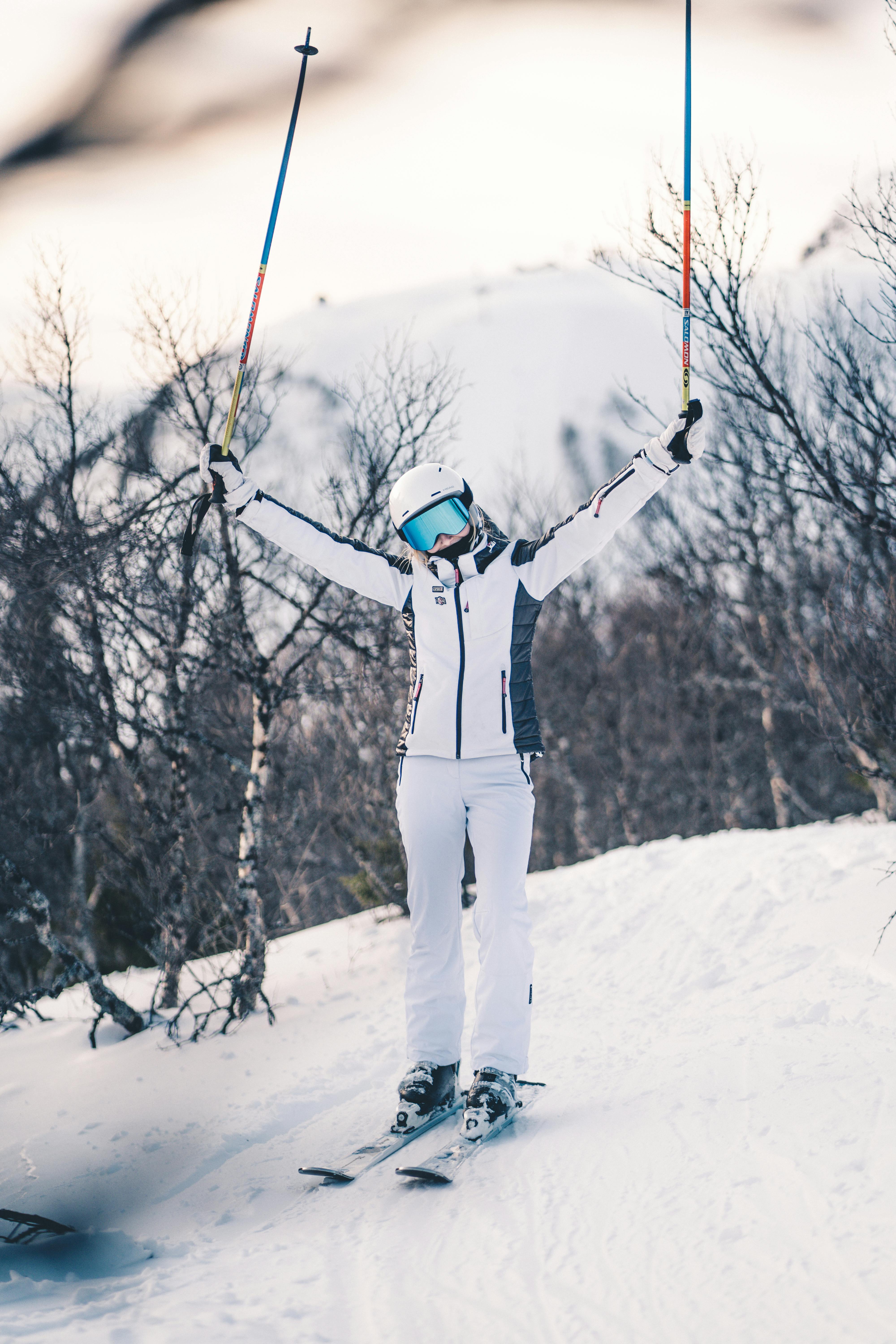 Prescription Goggle Inserts - A skier in winter gear raises ski poles triumphantly on a snow-covered slope surrounded by bare trees.