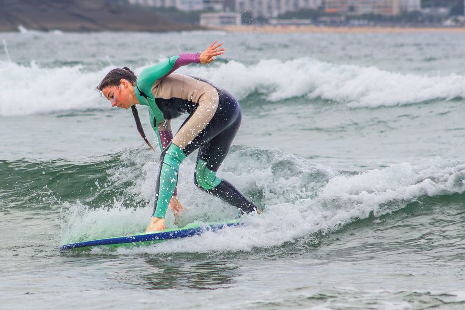 A woman in a wetsuit skillfully rides a wave on her surfboard, showcasing agility and balance.