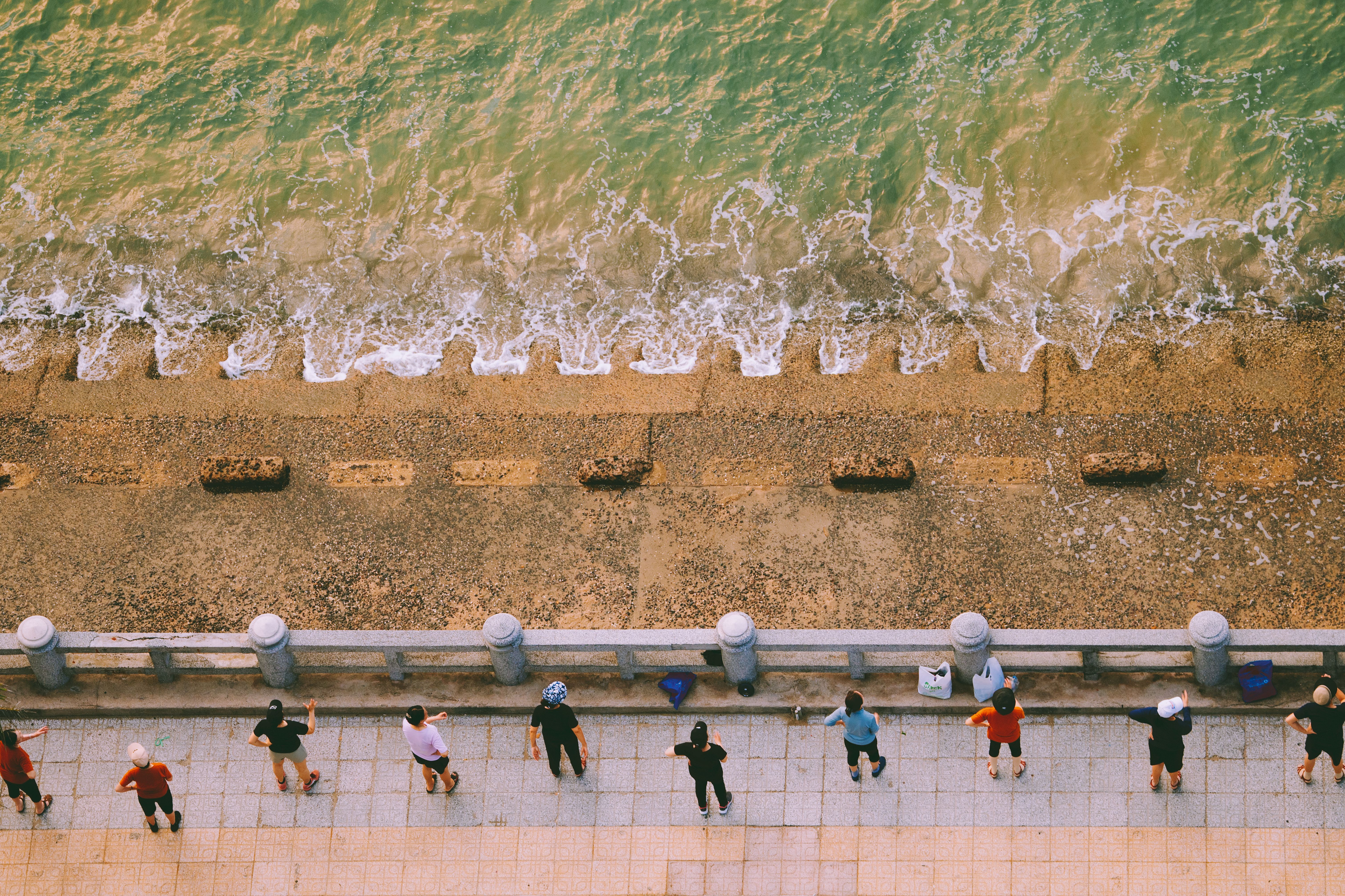 Aerial shot of a group exercising on a beach promenade with ocean waves.