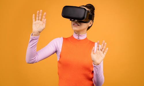 Woman in Orange and Pink Long Sleeve Shirt Wearing Black Virtual Reality Gadget