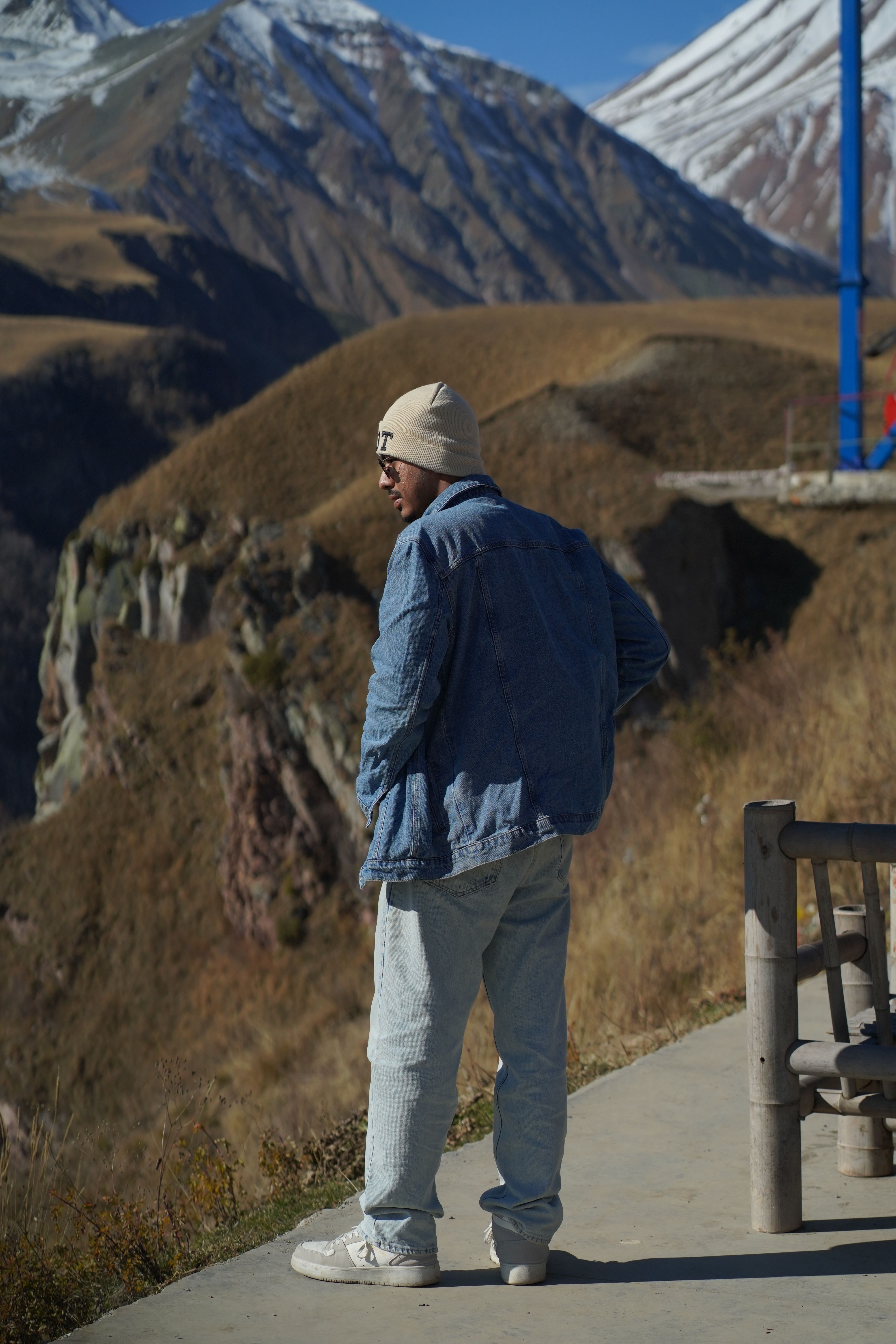 A man in casual attire stands on a mountain viewpoint in Georgia, enjoying the stunning scenery.