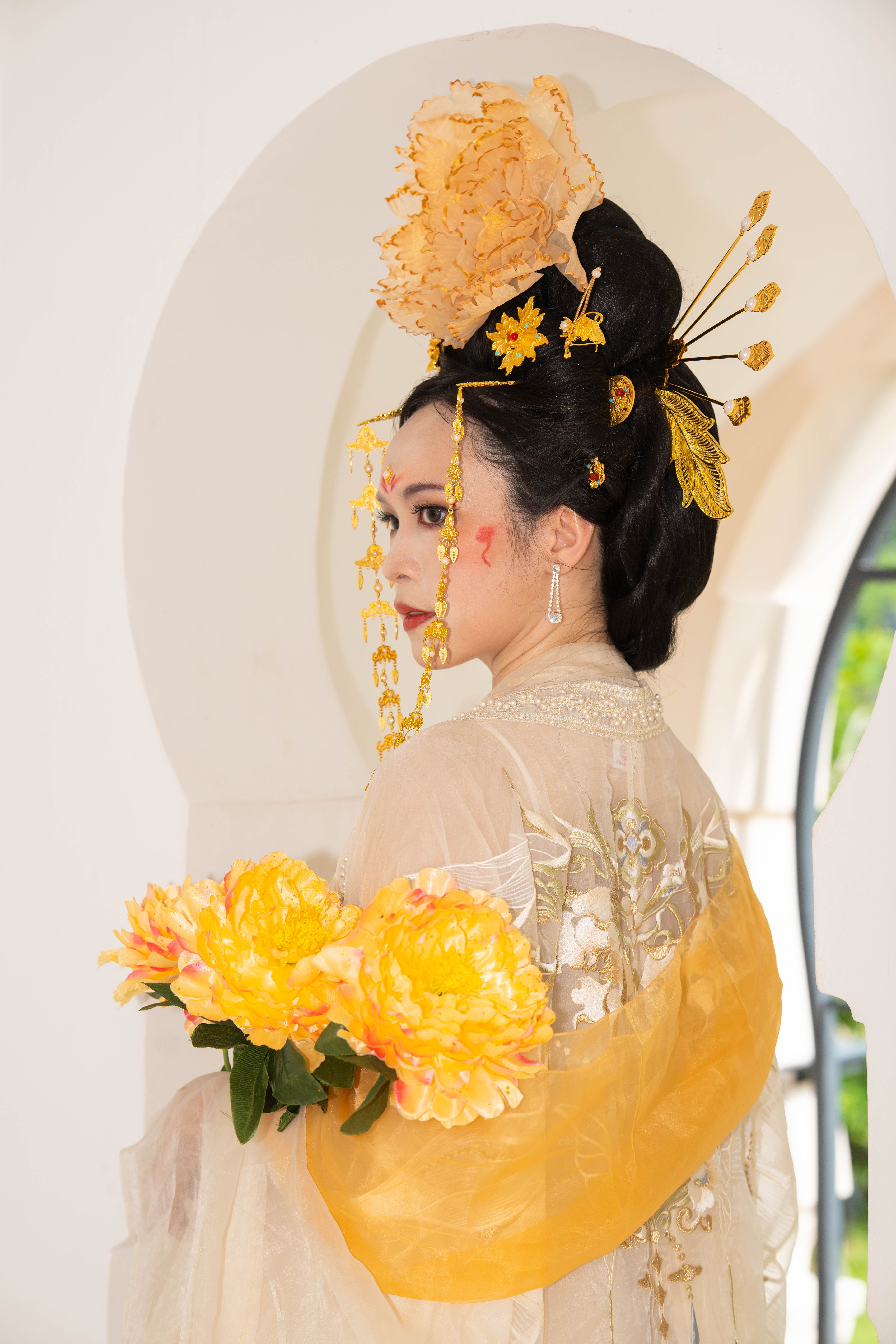 Elegant woman in traditional Asian attire holding flowers indoors.