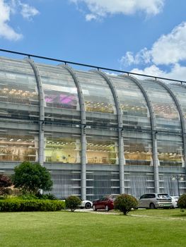 A sleek glass building with parked cars on a sunny day, showcasing modern architecture.