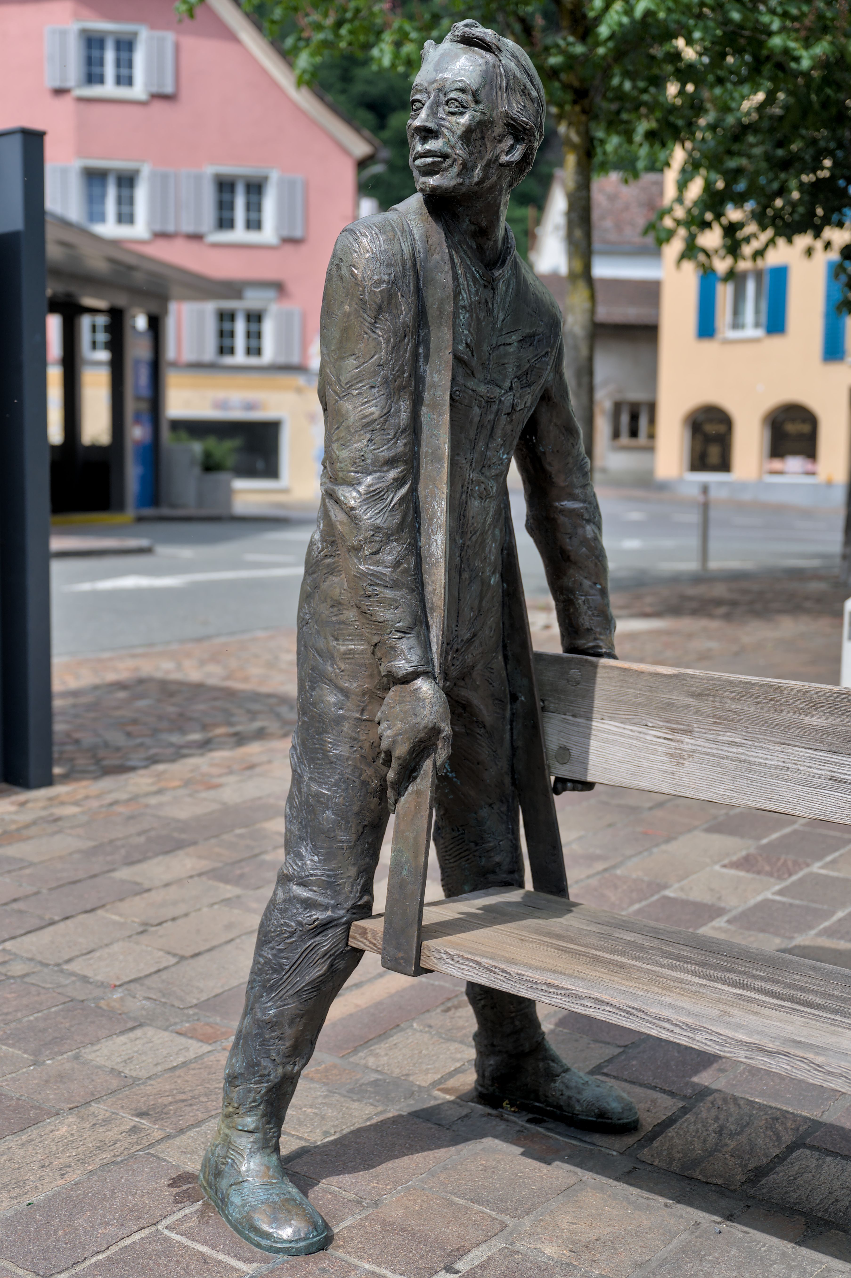 Bronze sculpture depicting a man with a bench in a charming European town street.