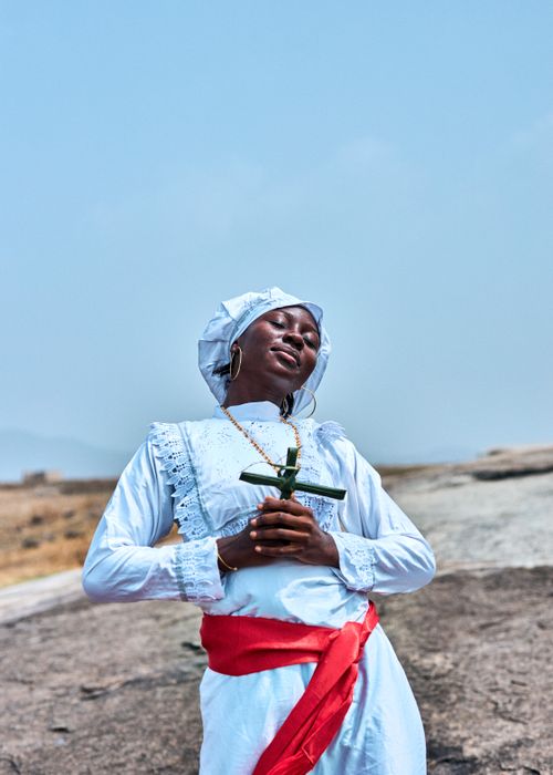 Free Young woman outdoors in traditional dress holding a cross, symbolizing faith. Stock Photo