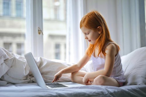 Beautiful Girl Sitting On White Bed Using Laptop 