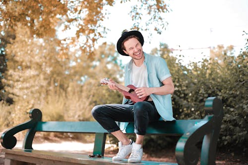 Man Sitting on Wooden Bench Using Ukulele