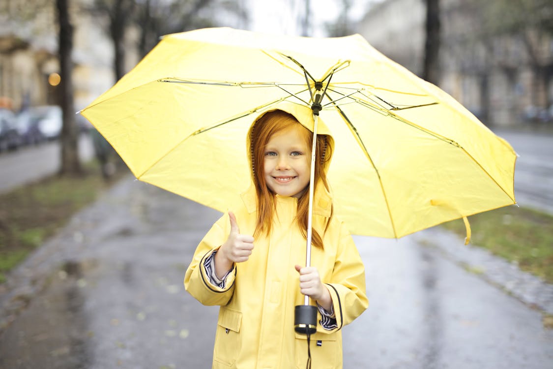 Free Foto Des Lächelnden Mädchens Im Gelben Regenmantel, Der Einen Gelben Regenschirm Hält, Während Man Einen Daumen Hoch Gibt Stock Photo