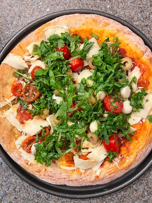Free Top-down view of a freshly baked homemade veggie pizza loaded with greens, tomatoes, and olives. Stock Photo