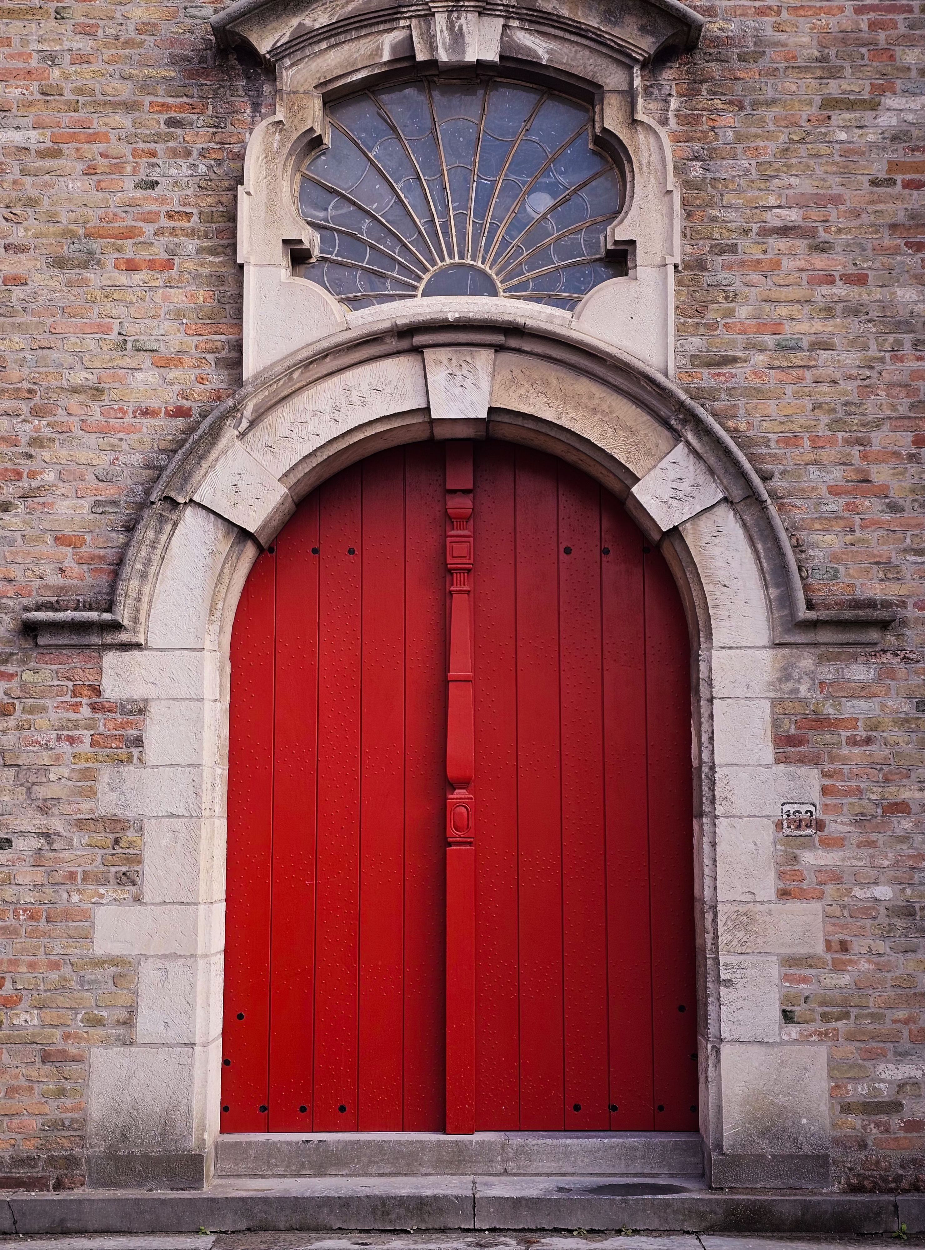 Charming red arched door set in a historic brick wall, perfect for architectural themes.