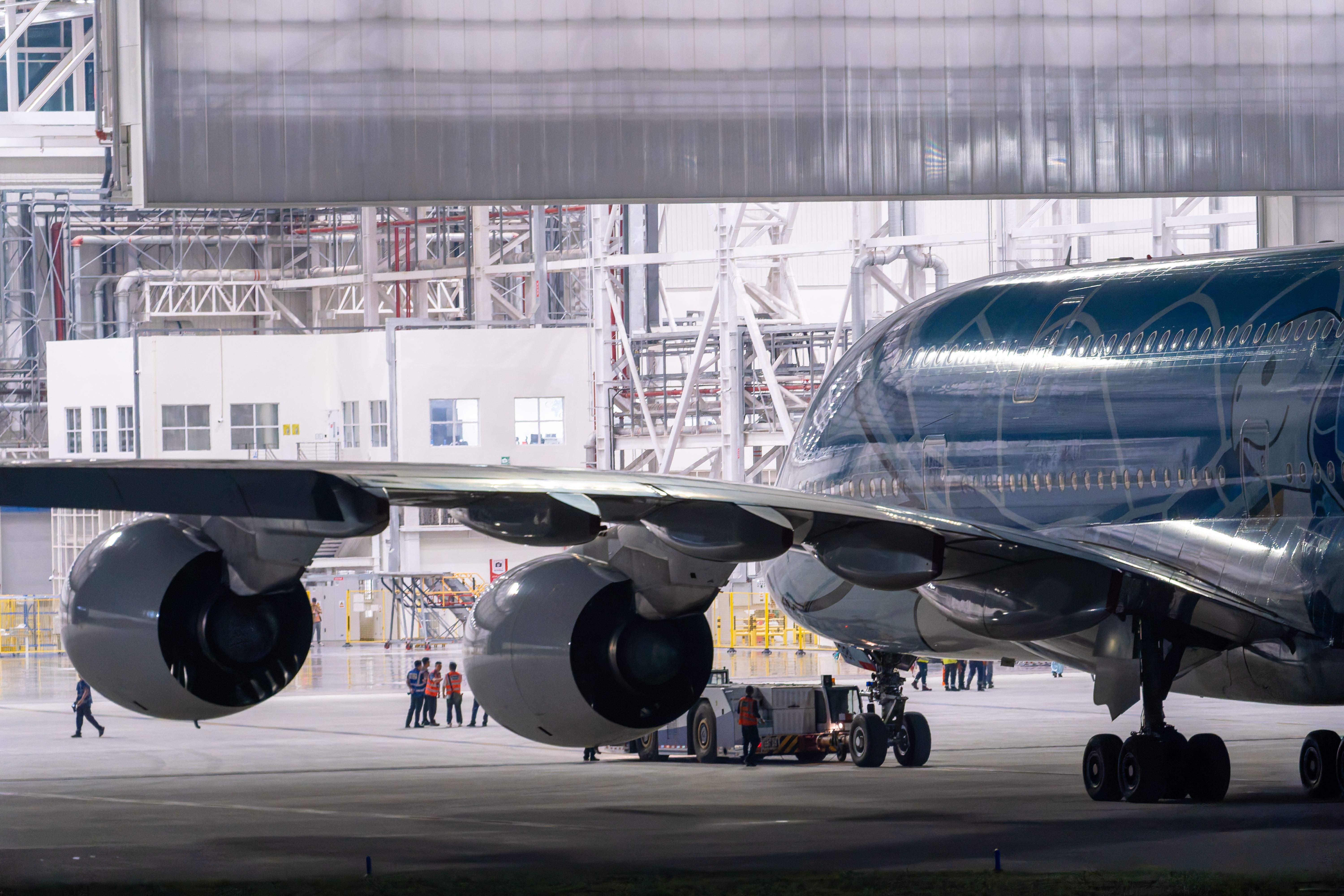 Engineering and maintenance crews work beneath the wing of a large commercial airplane inside an industrial hangar.