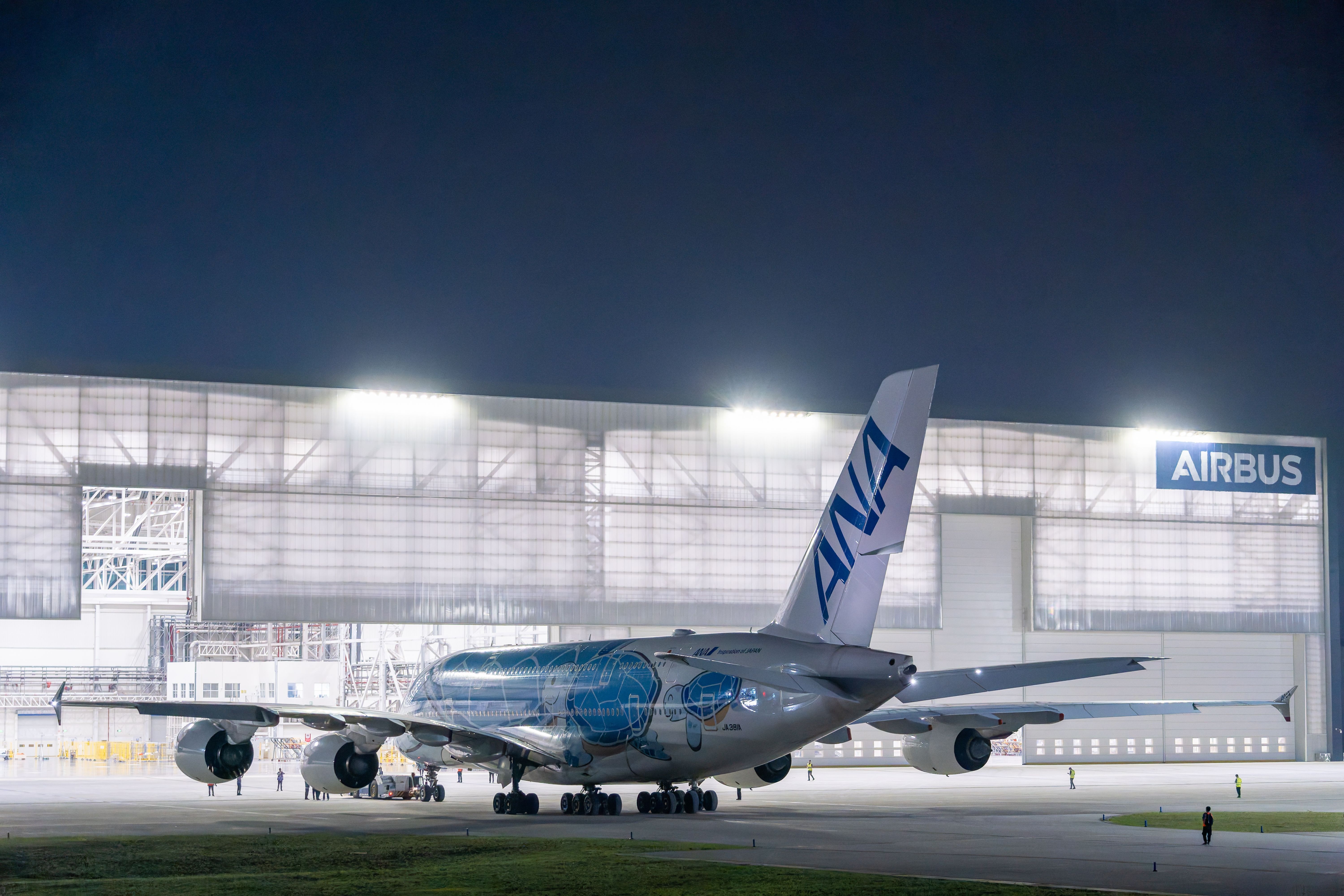 A large airplane parked at an Airbus hangar during nighttime, lit by bright lights.