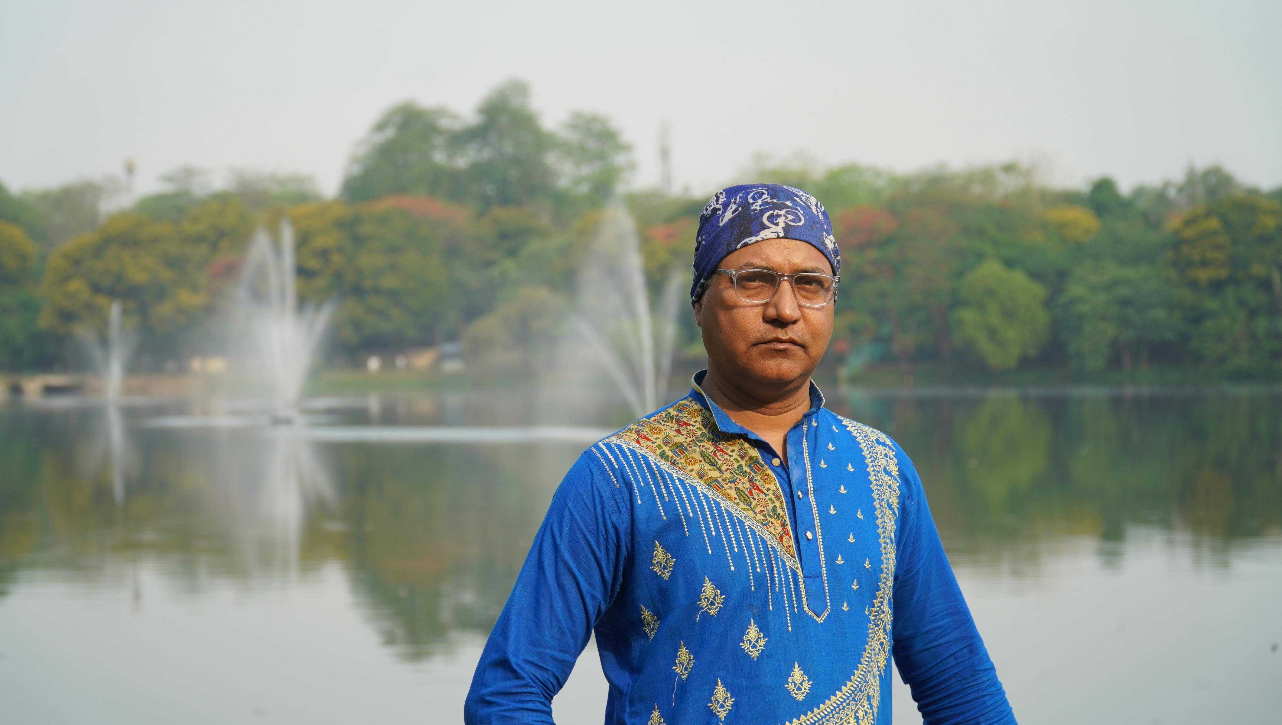 A man stands confidently by a lake with fountains in a Jamshedpur, India park.