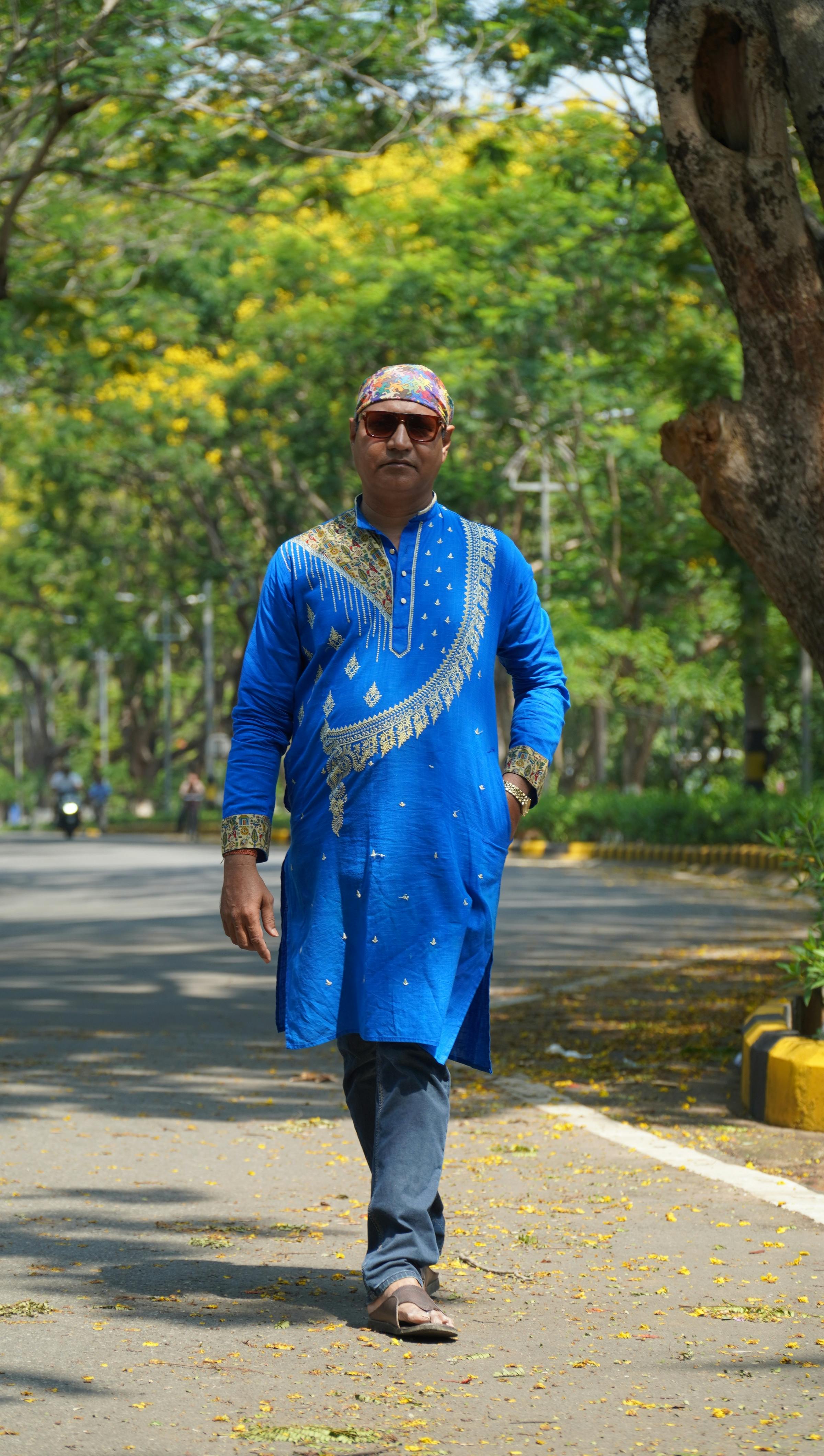 A man wearing a vibrant blue kurta walks along a tree-lined street in Jamshedpur, India.