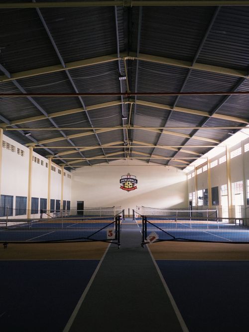 Free An empty indoor tennis court featuring pickleball branding under a metal roof. Stock Photo