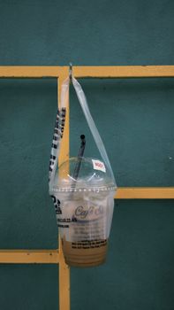 Iced coffee in a plastic bag hanging on a teal wall, offering a minimalist and urban aesthetic.