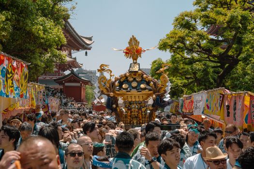 Crowds gather at Senso-ji Temple in Tokyo for a vibrant traditional festival, featuring colorful banners and mikoshi parade.