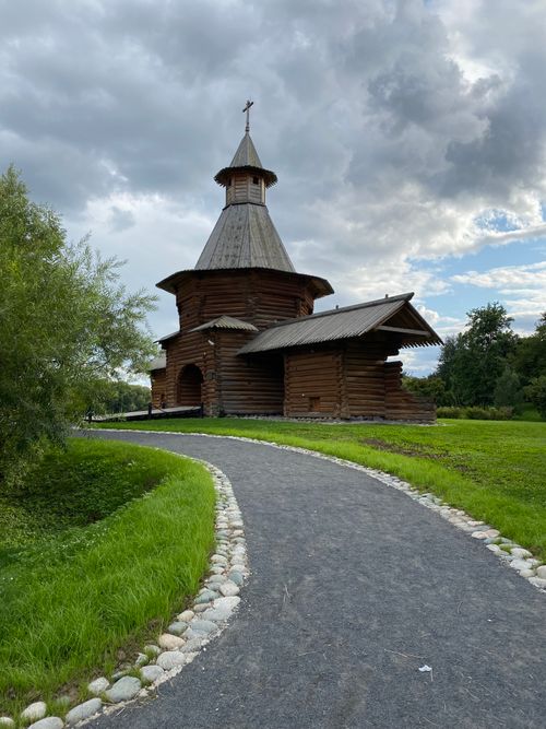 Free A picturesque wooden church nestled in a lush park under a dramatic cloudy sky. Stock Photo