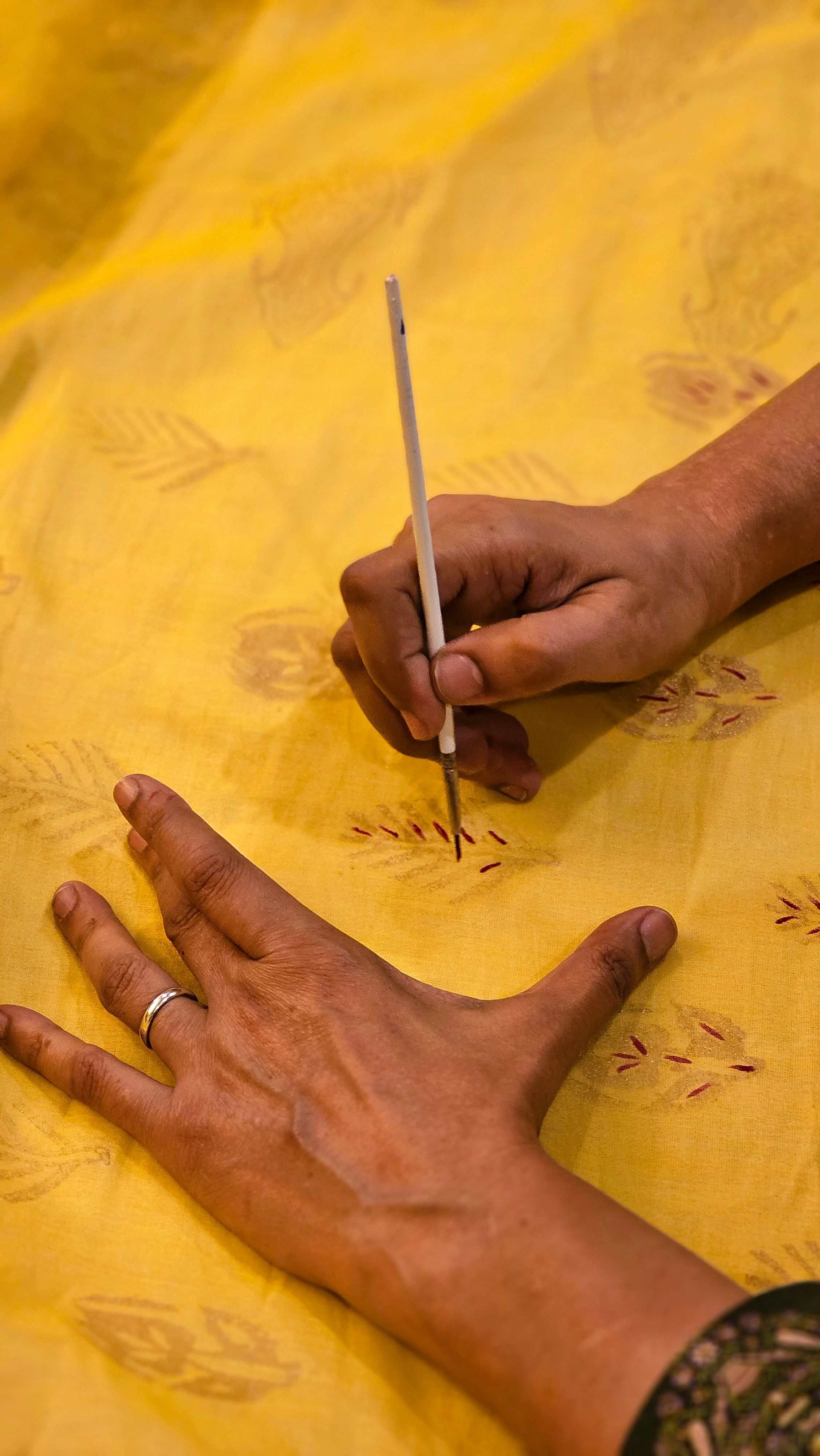 Close-up of an artisan hand-painting traditional patterns on fabric, showcasing craftsmanship.