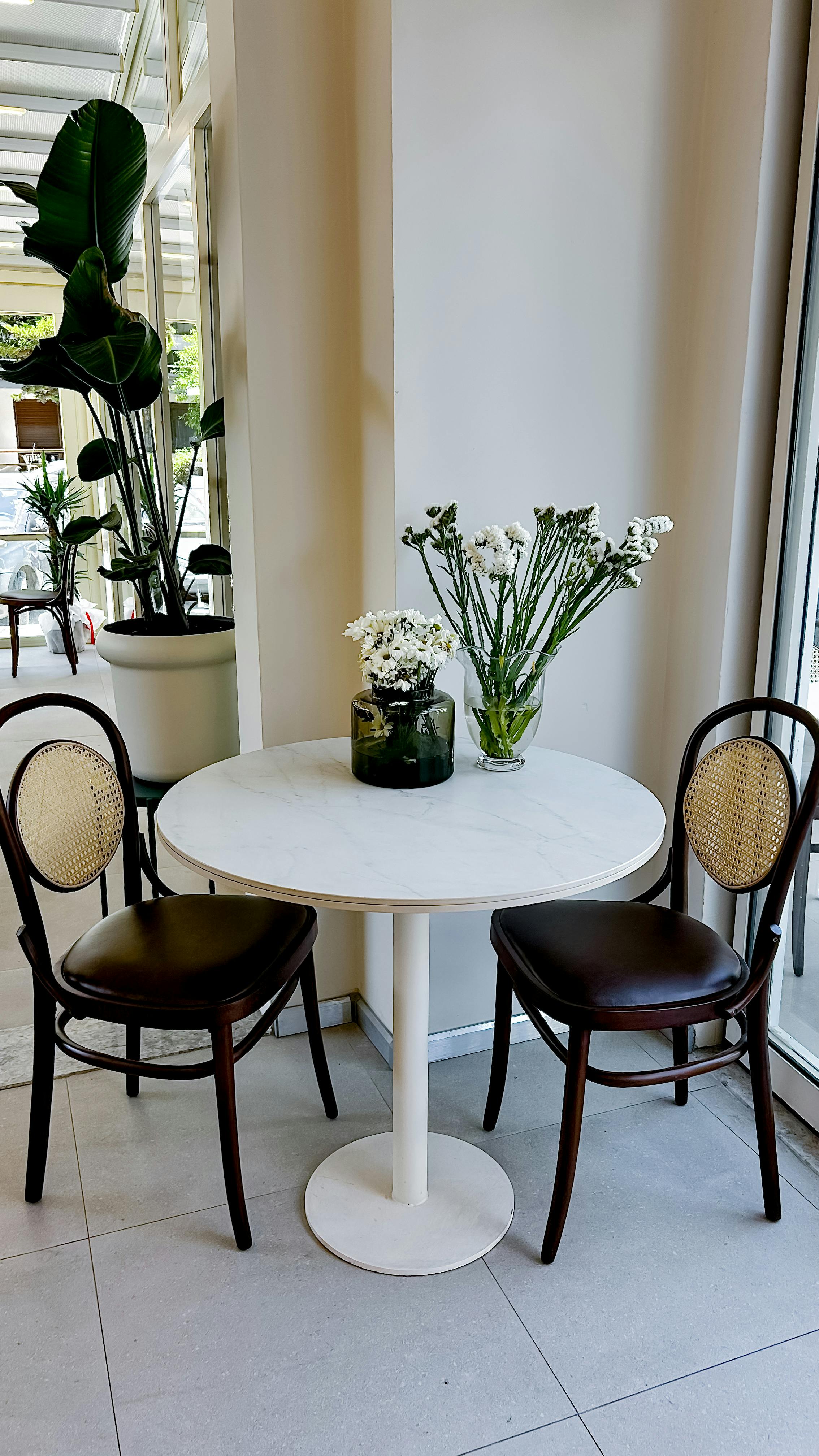 Cozy cafe setting with a white table, two chairs, and elegant flower arrangements.