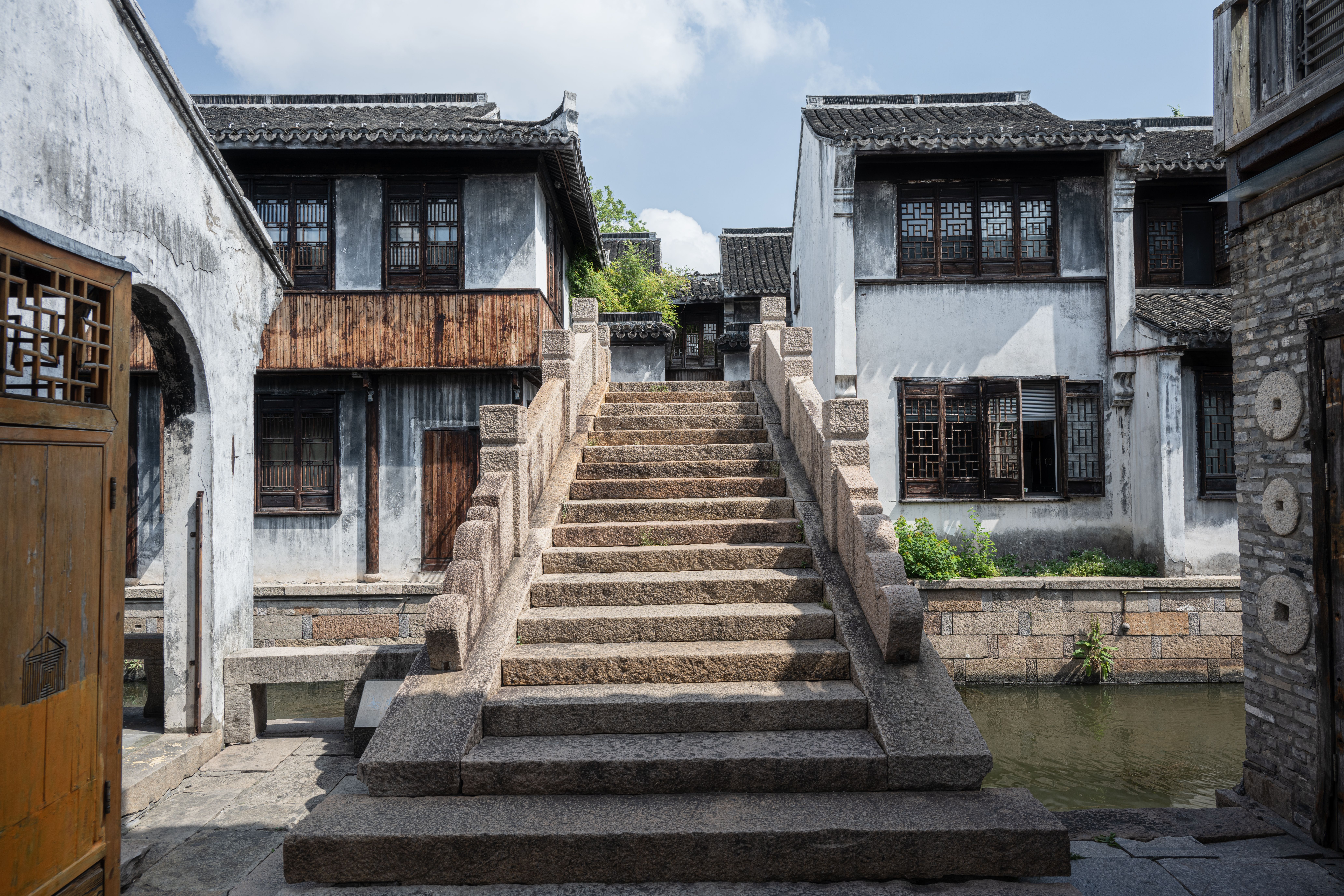 A canal alongside Pingjiang Road in Suzhou, with ancient stone bridges and white-walled buildings reflected in the water