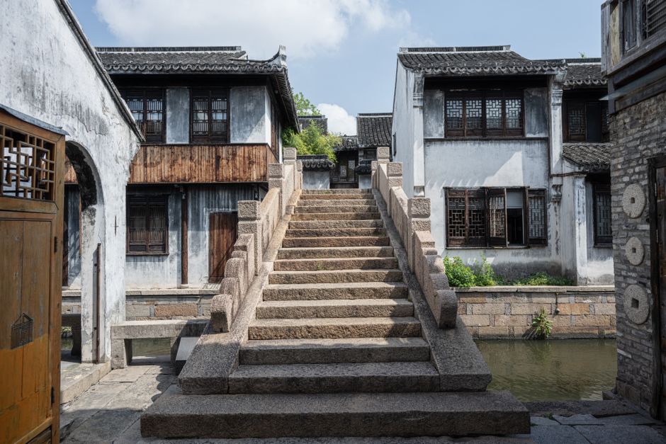 A canal alongside Pingjiang Road in Suzhou, with ancient stone bridges and white-walled buildings reflected in the water