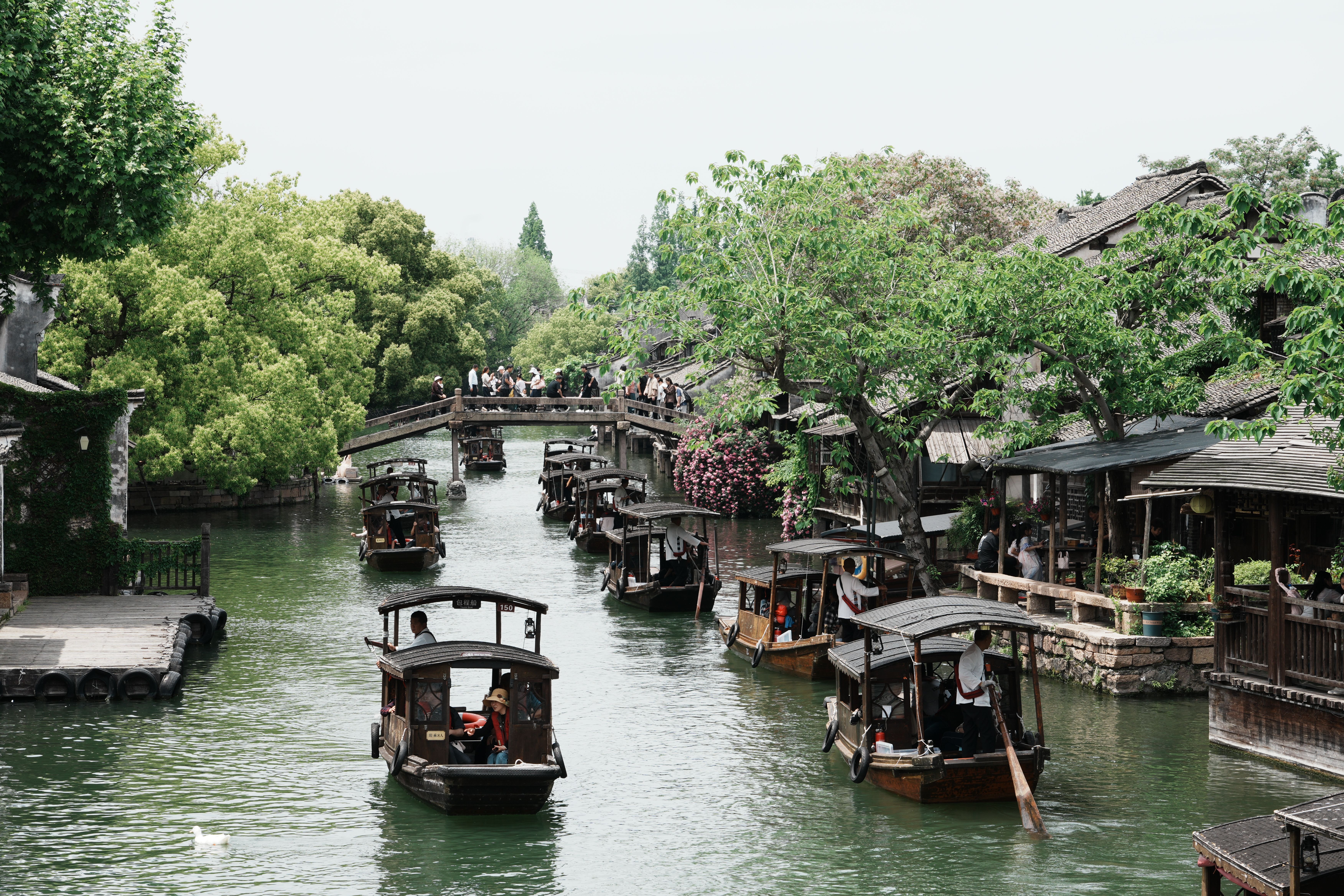 Traditional boats navigate a canal lined with trees and ancient architecture in Jiaxing, China.