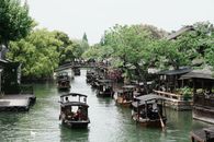Traditional boats navigate a canal lined with trees and ancient architecture in Jiaxing, China.