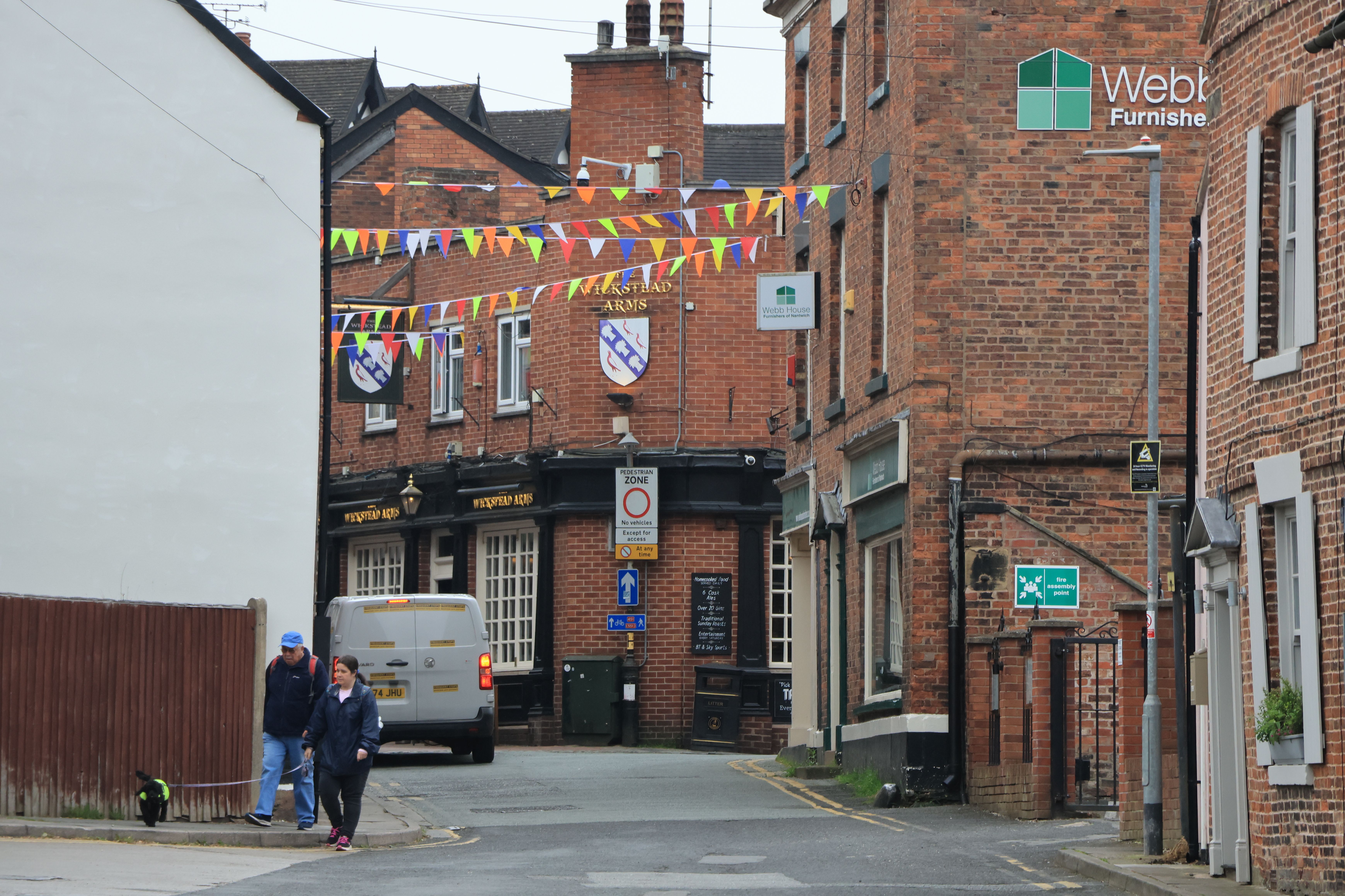 Quaint Nantwich street with colorful bunting, brick buildings, and pedestrians.