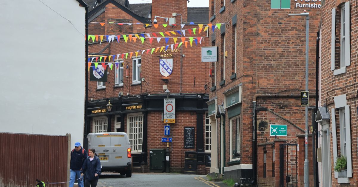 Quaint Nantwich street with colorful bunting, brick buildings, and pedestrians.