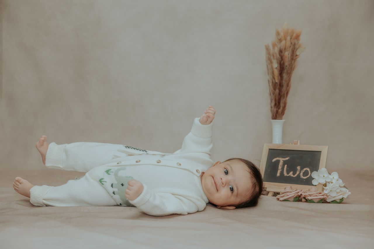 a cute two month old baby lies on a soft surface with a sign reading t