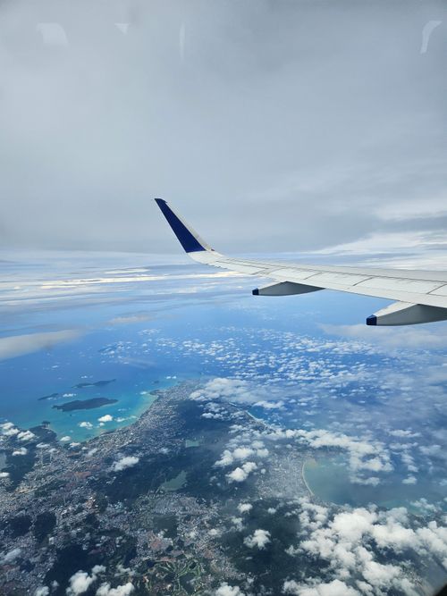 Free A breathtaking aerial view of Krabi's coastline, showcasing a plane wing over the blue sea and cloudscape. Stock Photo