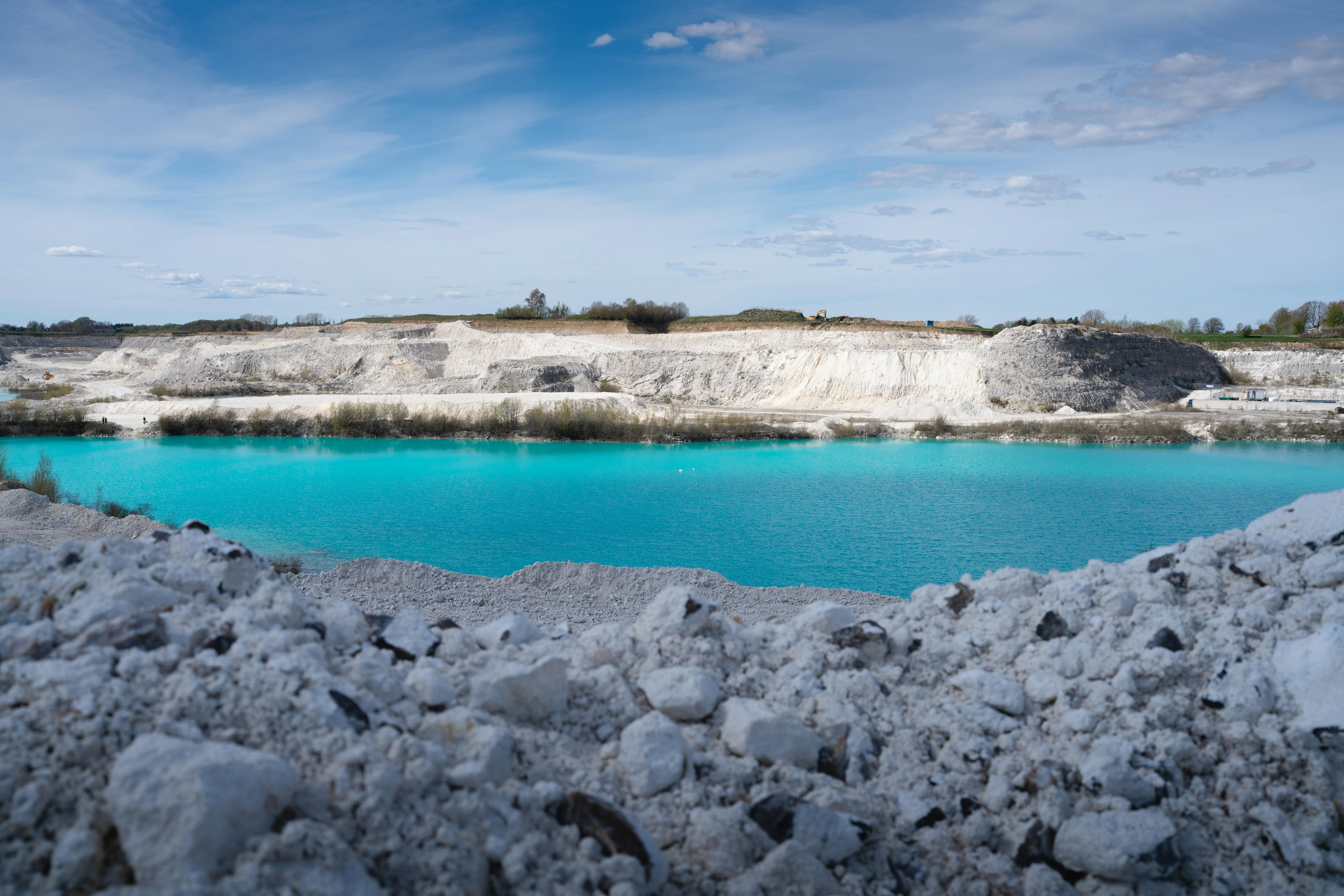 Stunning turquoise lake in a quarry with rocky terrain and clear blue sky.