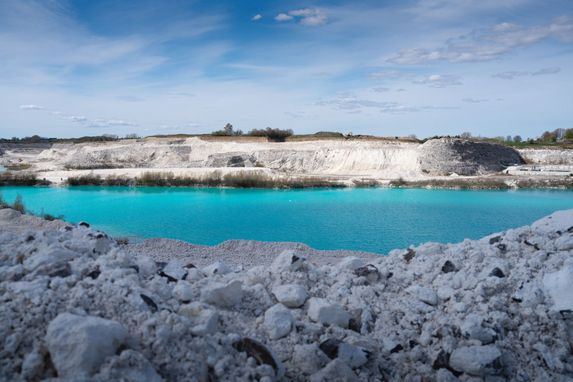 Stunning turquoise lake in a quarry with rocky terrain and clear blue sky.