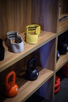 Vibrant gym equipment including kettlebells and resistance bands neatly arranged on wooden shelves.