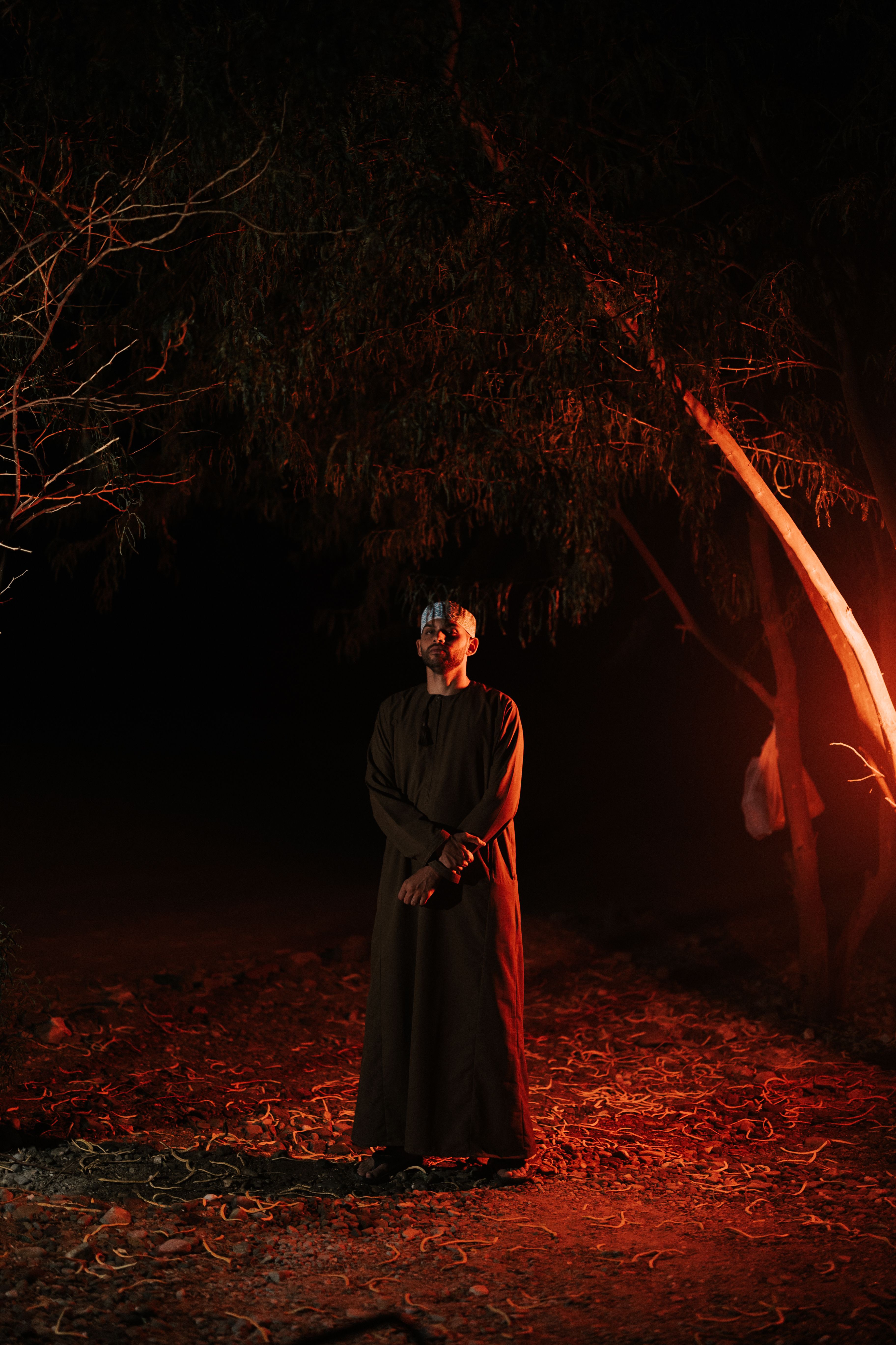 A dramatic portrait of a man in traditional attire under a tree at night in Oman.