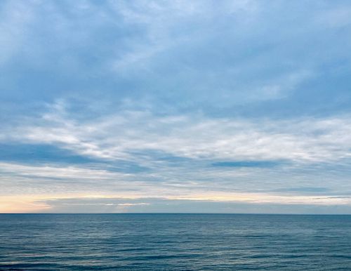 Free Calm ocean meeting a cloudy sky at sunrise, with a hint of orange on the horizon. Stock Photo
