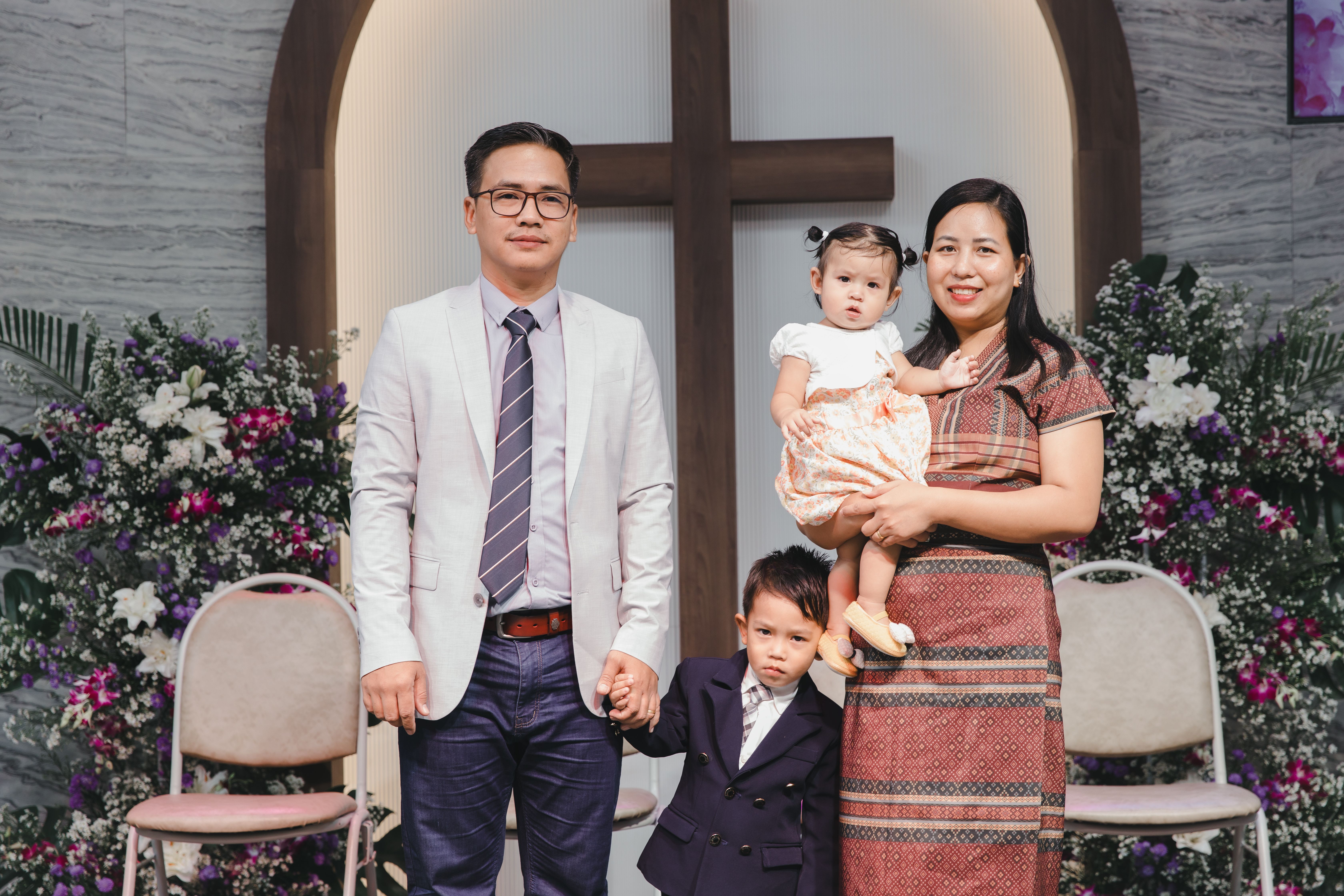 Family posing indoors with floral backdrop and cross in a church.