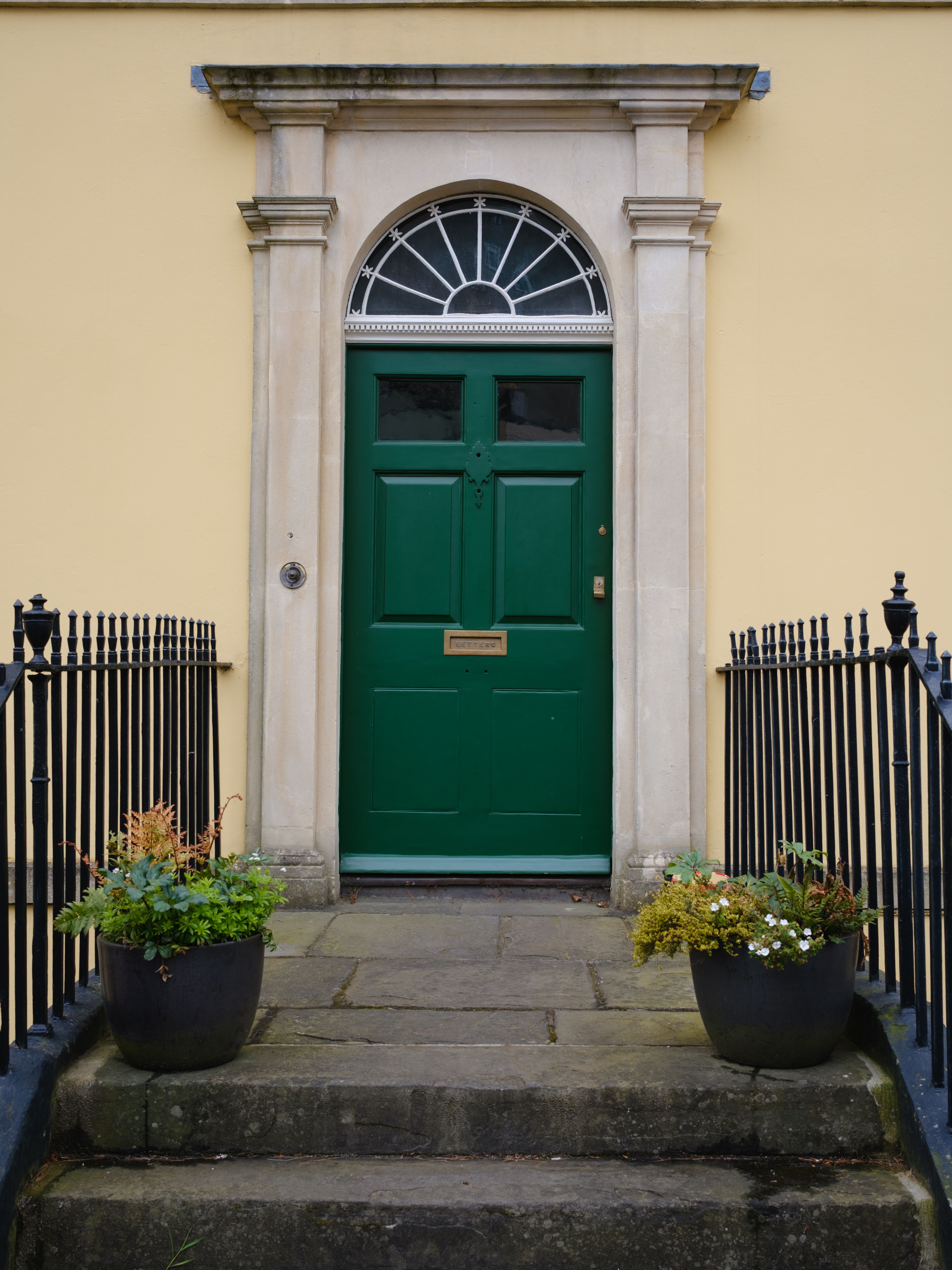 Elegant green door in classic Georgian style, adorned with potted plants, UK.