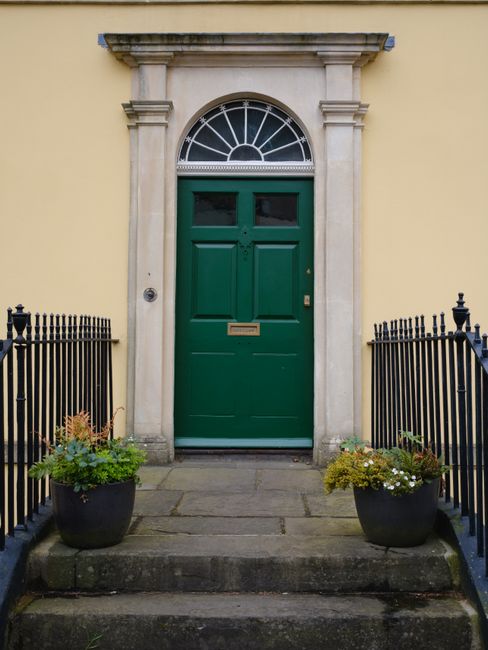 Elegant green door in classic Georgian style, adorned with potted plants, UK.