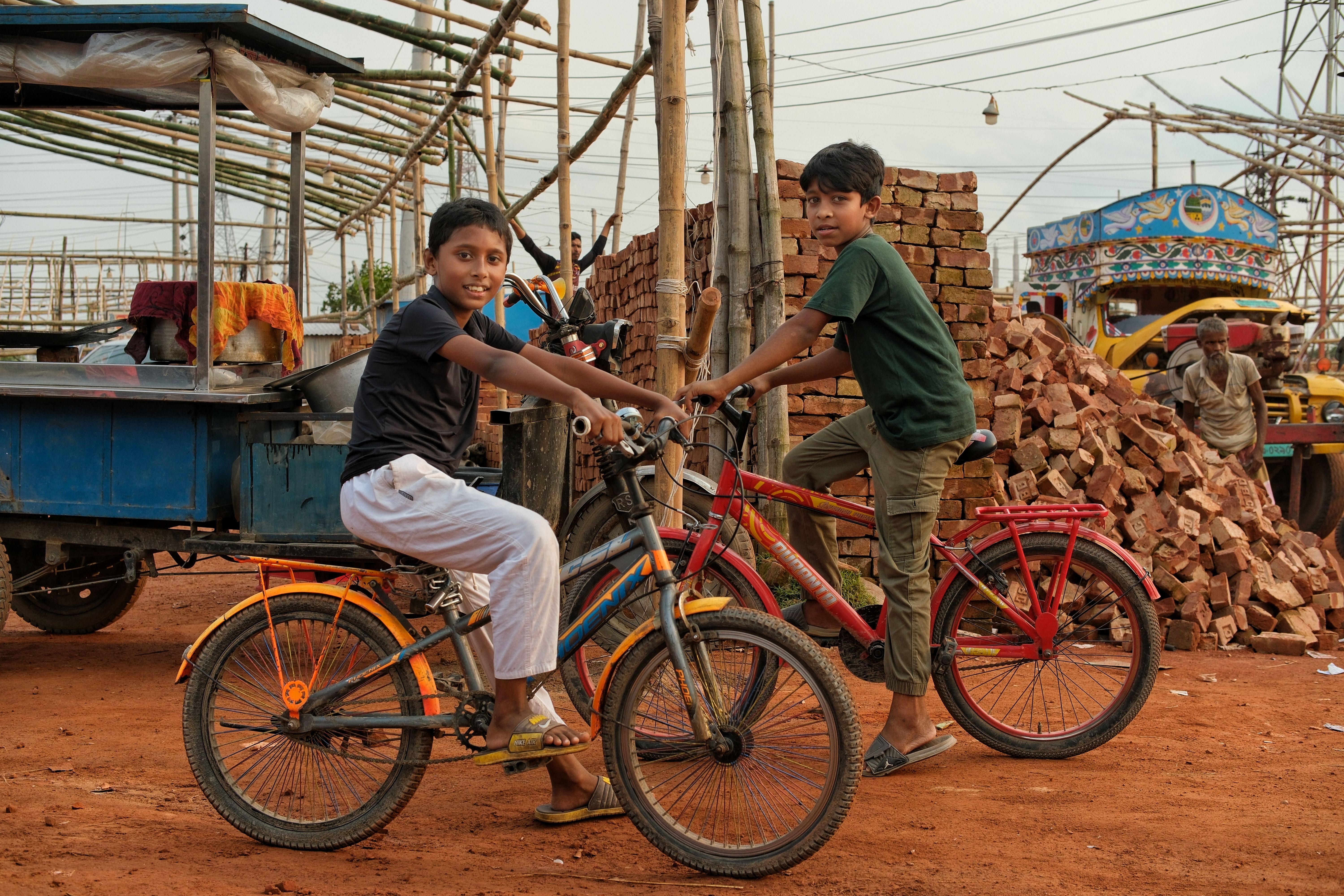 Young boys enjoying a bicycle ride amidst a lively market scene in Gabtali, Bangladesh.