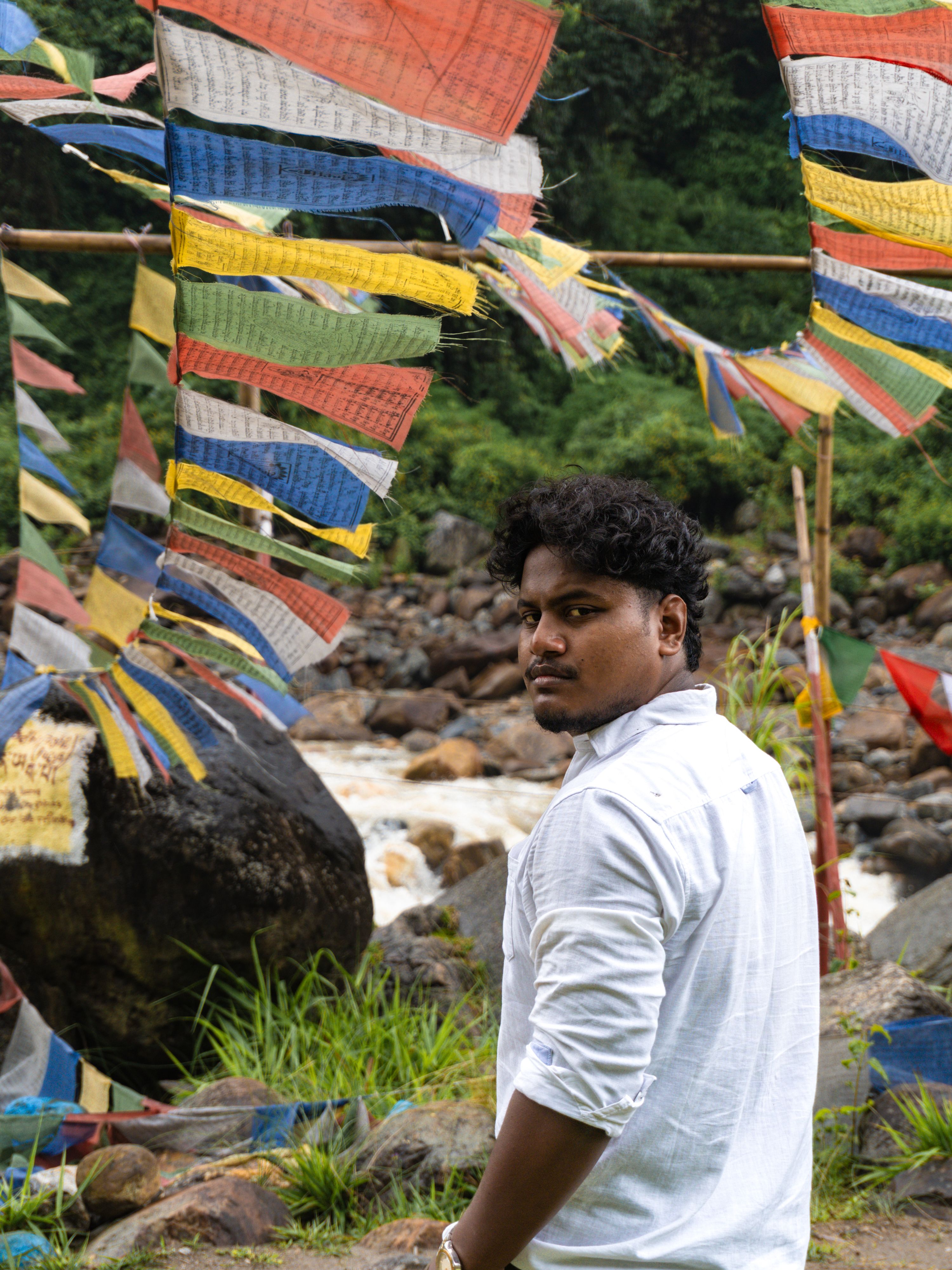 Portrait of a man standing by colorful prayer flags near a flowing river.