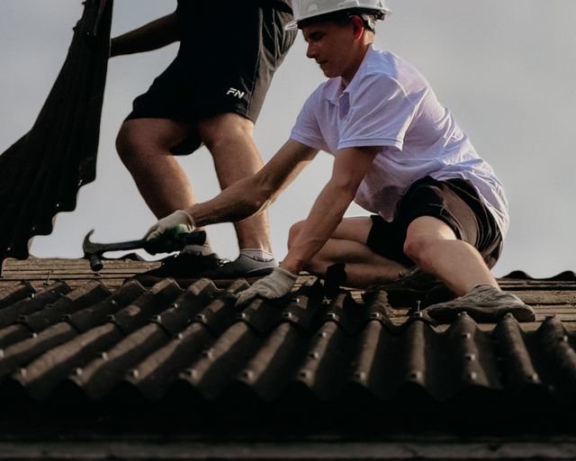 Roofers fixing roof tiles Two roofers in helmets fixing roof tiles on a sunny day